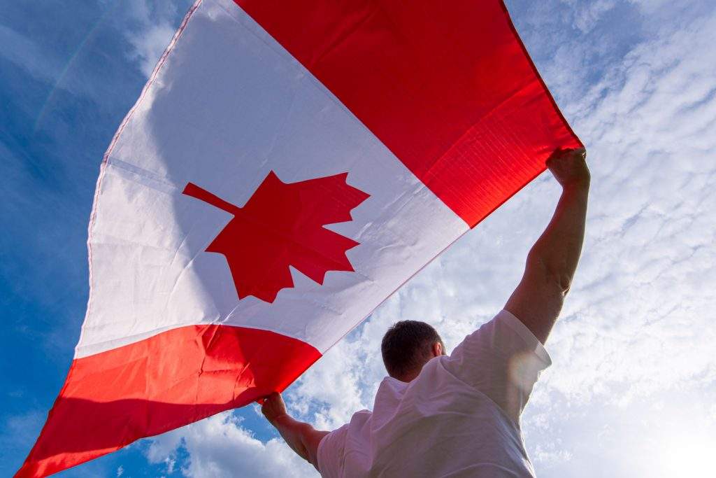 man-holding-national-flag-canada-against-blue-sky